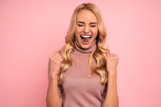 Portrait of beautiful joyous woman screaming and gesturing as winner isolated over pink background in studio