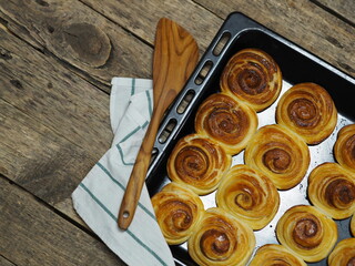 Freshly baked homemade cinnamon rolls lie on a baking sheet from the kitchen oven against a wooden ancient background.Food background.