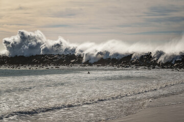 Stormy ocean at high tide, rocky beach, and silhouette of surfer, Morro Bay, California