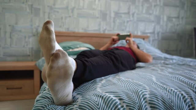 a man in dirty socks lies on the bed and uses the phone