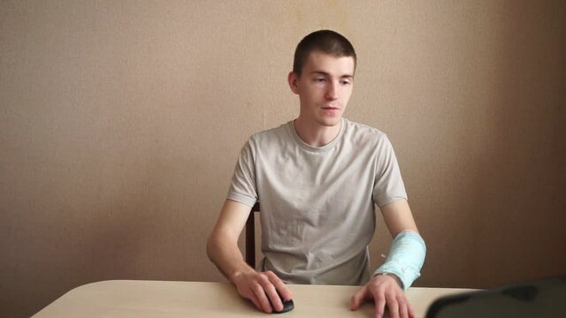 a guy sits at a laptop teaches with a bandaged hand, a small bruise on his hand