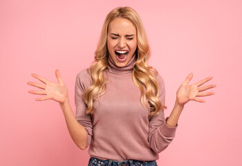 Fototapeta na wymiar Confused screaming blonde woman in sweater with closed eyes over pink background