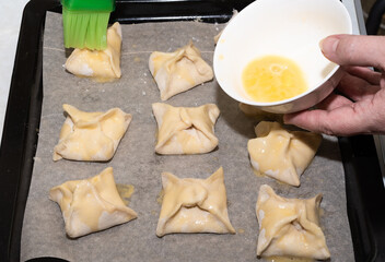 Smearing egg yolk on puff pastry envelopes before baking in the oven. Close up. Copy space.