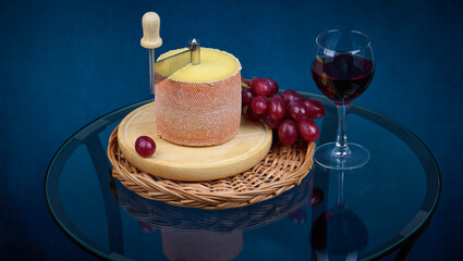 Gourmet tasty cheese Tete de Moine, a glass of red wine and a bunch of grapes on a glass table, shallow depth of sharpness