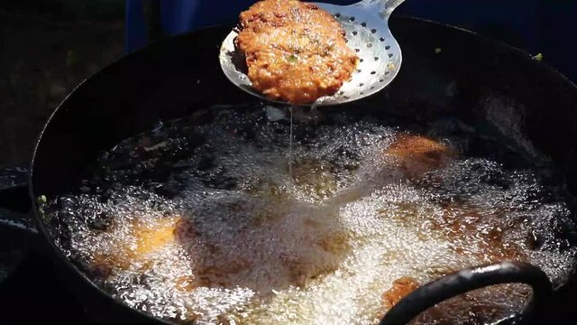 Deep Frying Traditional South Indian Food Masala Daal Vada Also Known As Parippu Dal Wada Made Of Split Bengal Gram Pulse In Black Wok Kadhai And Taking Out The Fried Snacks Using Palta Or Turner