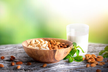 Almonds or nuts in brown bowl with glass of milk on wooden vintage table.