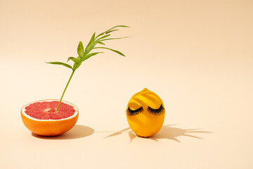 Yellow vibrant lemon in a palm leaf shade next to a juicy grapefruit on a pastel tan colour background. Creative art concept.