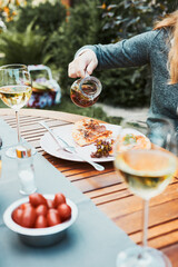 Family and friends having meal - pizza, salads, fruits and drinking white wine during summer picnic outdoor dinner in a home garden. Close up of people sitting at the table in a orchard in a backyard
