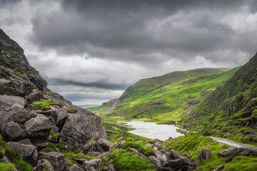 Fototapeta na wymiar Panoramic view on green mountain hills and a lake in Gap of Dunloe. Dramatic stormy sky in Black Valley, Ring of Kerry, County Kerry, Ireland