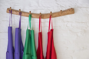 Coloured cooking aprons hung up on wooden pegs