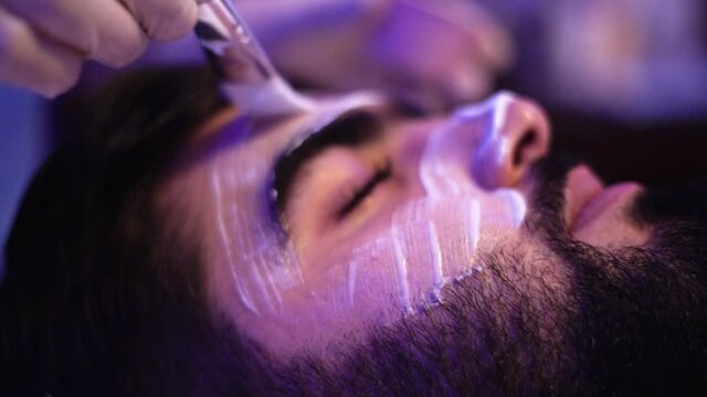  Bearded mature man getting facial mask treatment at spa centre. Resort, recreation concept