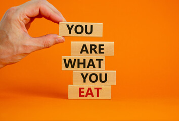 You are what you eat symbol. Stack of wooden blocks. Words 'You are what you eat'. Male hand. Beautiful orange background. Healthy eating concept. Copy space.