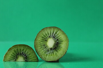 half and a circle of kiwi kusrchek with reflection on a green background with a copyspace