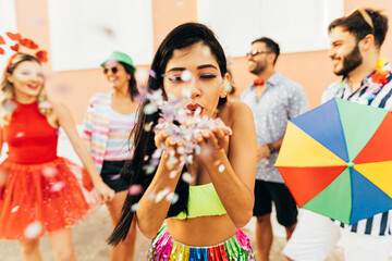 Brazilian Carnival. Young woman enjoying the carnival party blowing confetti