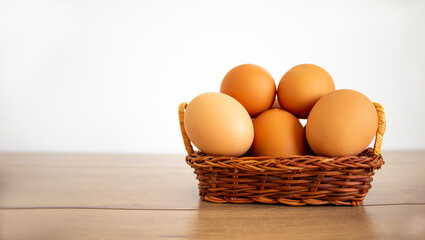 Chicken eggs in a wicker basket. Raw eggs in basket on wooden table. Beautiful white background, copy space. Concept.