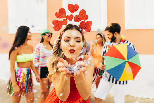 Brazilian Carnival. Young woman enjoying the carnival party blowing confetti