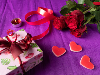 White gift next to hearts and ribbon and red roses