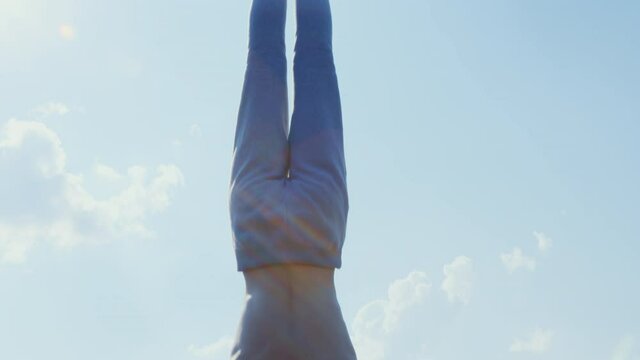 A man does a street workout at a sports ground. A sportsman does a handstand on parallel bars against an urban landscape