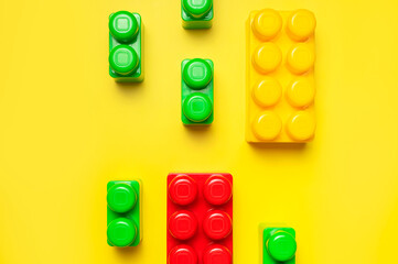 Multicolored plastic kids constructor on yellow background. Colored children's bricks for construction. Flat lay top view copy space. Plastic building blocks background. Developing toys, game