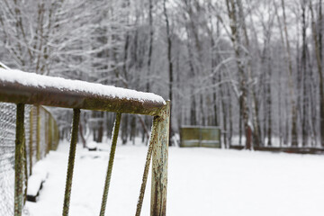 Rusty metallic gate covered with white snow with snowy forest on a background