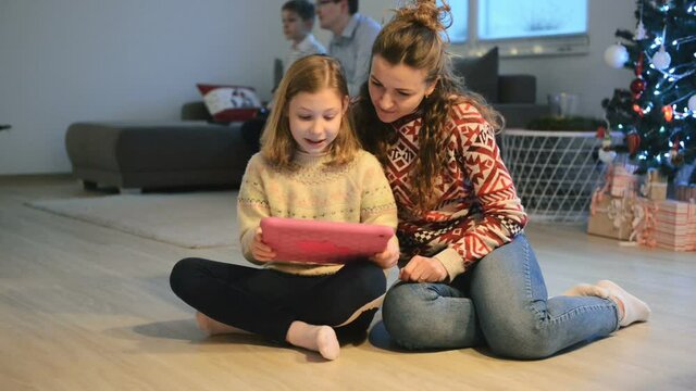 Happy mother with beautiful daughter playing with tablet. Father with son playing console on sofa on background