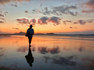 Silhouette of young woman walking on the beach at amazing sunset.