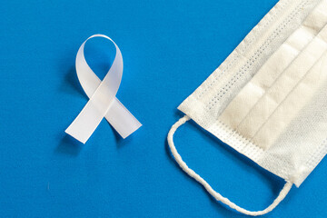 white tape and face protection mask on blue background. the white ribbon represents a mental health...