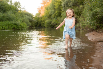 a little girl runs in the river in shallow water along the shore. She laughs and has fun