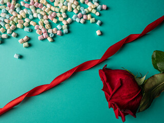 Red rose and multicolored candies and between them lies a red long ribbon