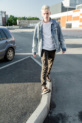 a young guy in a denim jacket walks through the parking lot with white hair confidently