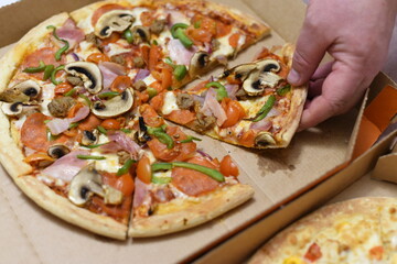 A hand pulls a slice of delicious hot freshly made pizza out of the box.
