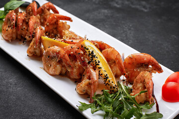Fried shrimps in garlic-soy sauce, with sesame seeds, on a white plate, on a dark background
