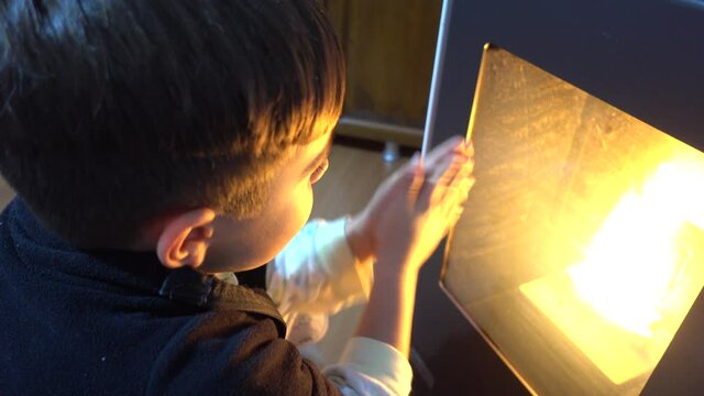 4K Child rubs and warms up his hands against the fire in furnace
