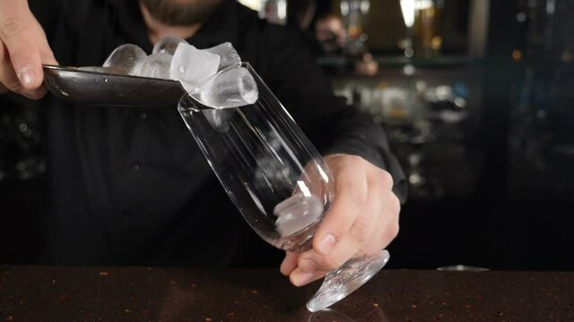 Ice cubes falling into empty transparent glass. Barmen making cocktail. Slow motion. Making refreshing drink. Cooking delicious cocktails on restaurant bar counter. Full hd