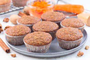 Homemade carrot cake muffins with walnuts on gray plate and cooling rack, horizontal