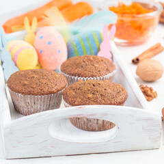 Homemade carrot cake and walnut muffins on a wooden tray with Easter eggs, bunnies and feathers, square