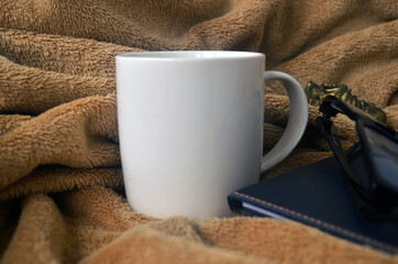 White mug with coffee and steam on a brown plaid, book, notebook