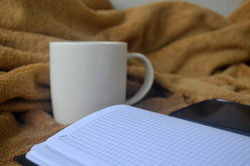 White mug with coffee and steam on a brown plaid, book, notebook