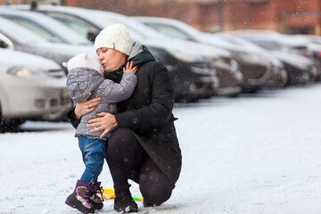 Fototapeta na wymiar Mother talking with her little child, embracing and kissing after falling dawn on ice at winter season