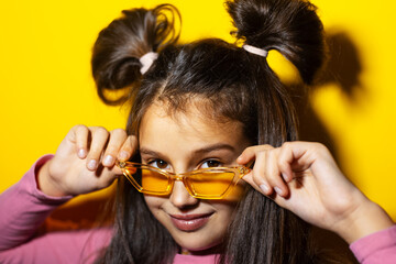 Studio portrait of cheerful teenage girl with glasses on yellow background.