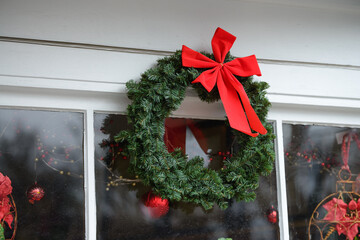 Christmas wreath with a red bow and other decorations in a window on a storefront.