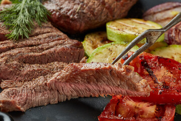 Grilled beef steak with spices and vegetables. Selective focus on slice of meat on fork