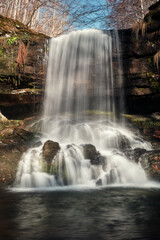 Low angle view of scenic, powerful waterfall with blurred motion water splashing on the wet, dark red rocks covered by colorful moss © Nikola