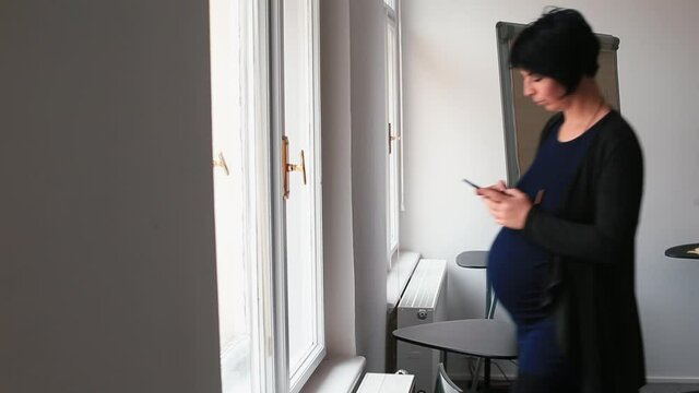 Pregnant woman with smartphone comes to window to call doctor. Monitoring of training contractions in last trimester of pregnancy. Remote observation of development of palate use telecommunications.