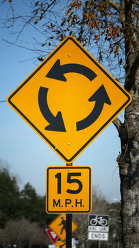 North American roundabout sign with arrows and 15 miles per hour speed limit indication