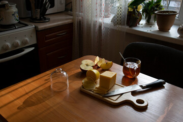 Table in the kitchen with breakfast. Tea, cheese, lemon, apple.