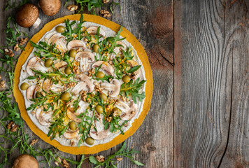 Delicious raw pizza with mushrooms, walnuts, arugula and green olives. Top view.