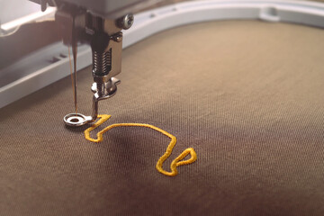 Needle bar of an embroidery machine moves down fast to stitch ox symbol on shiny olive green fabric...