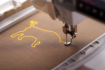 top view on embroidery machine stitching the head of an ox symbol on shiny olive green fabric with golden yarn in bright sunny light - selective focus chinese new year concept