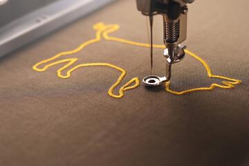 The embroidery of an golden ox symbol on shiny olive green fabric is nearly finished by an modern...